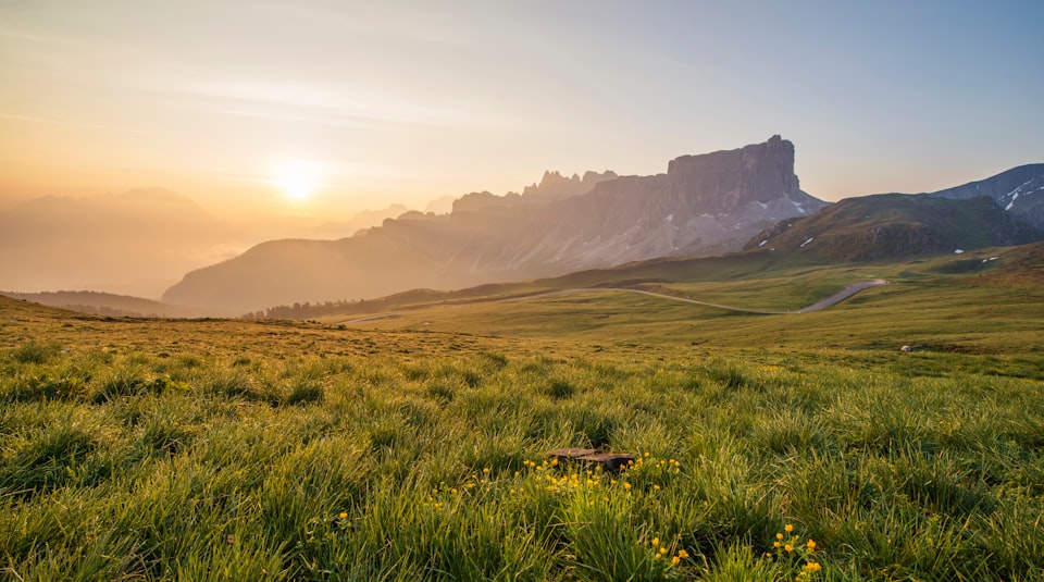 Landscape photo of a sunrise over a field with crags in the distance.