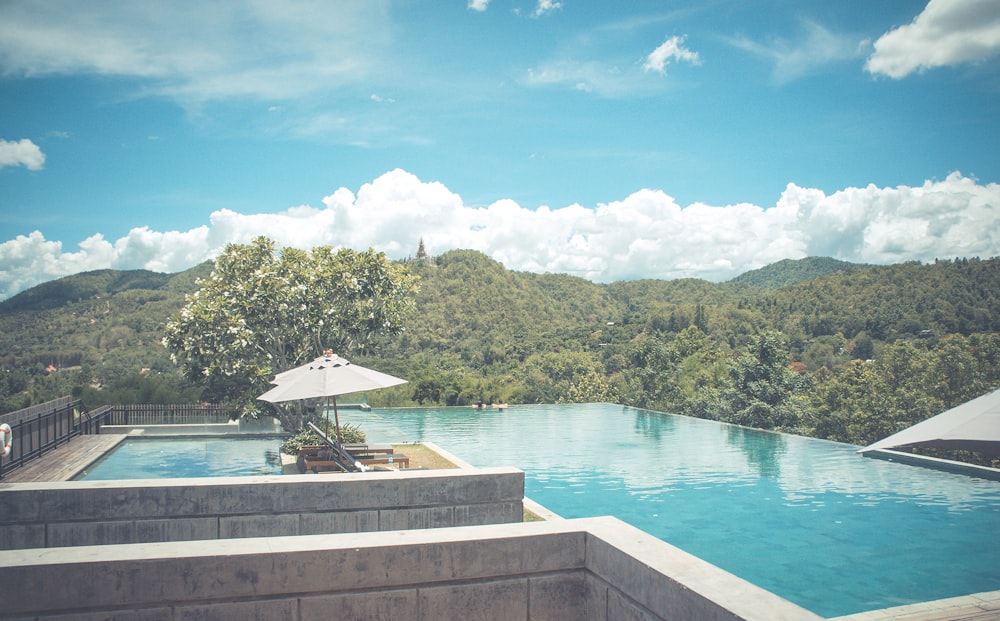 white parasol on the center of swimming pool with green leafed trees in distant