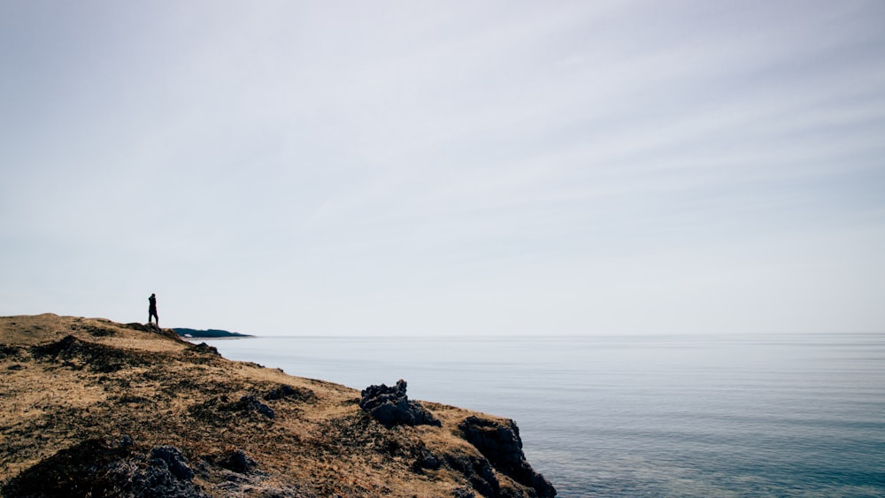 silhouette of person standing on mountain cliff near sea