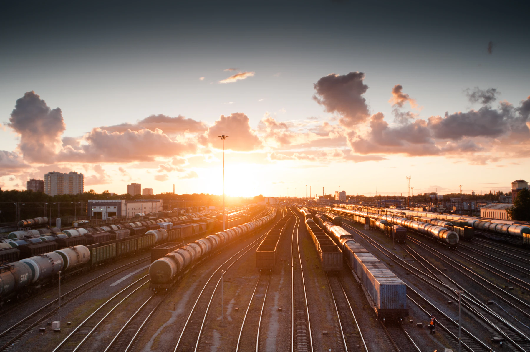 A wide rail yard seen from above at sunset, rows of tank cars and freight cars on a dozen tracks