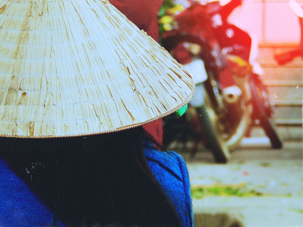 Persona con sombrero de arroz frente a una motocicleta blanca estacionada junto a la pared roja