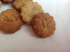 A collection of round, rustic crackers with a rough texture and visible herbs, resting on a pale, textured fabric background.