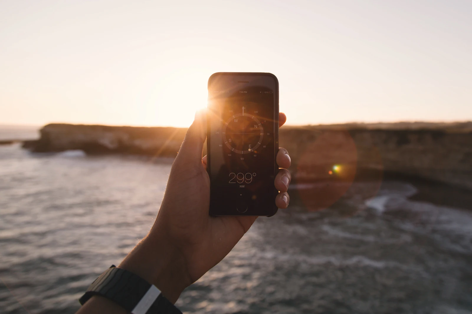 Hand holding a smartphone against a golden sunset over the sea while checking APN settings on a travel eSIM