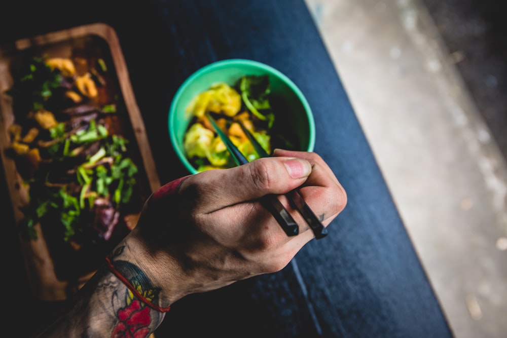 person holding chopsticks near green bowl