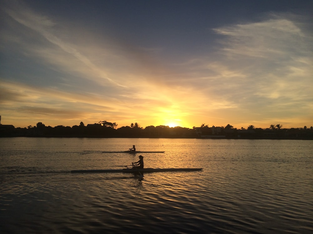 two people silhouette on body of water during golden hour