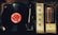 A vintage record player with a spinning vinyl record on the left side. The record has a bright red label. To the right, an analog radio tuner with dials for selector, balance, tone, loudness, and tuning is visible. The tuner displays frequencies with an illuminated red indicator.