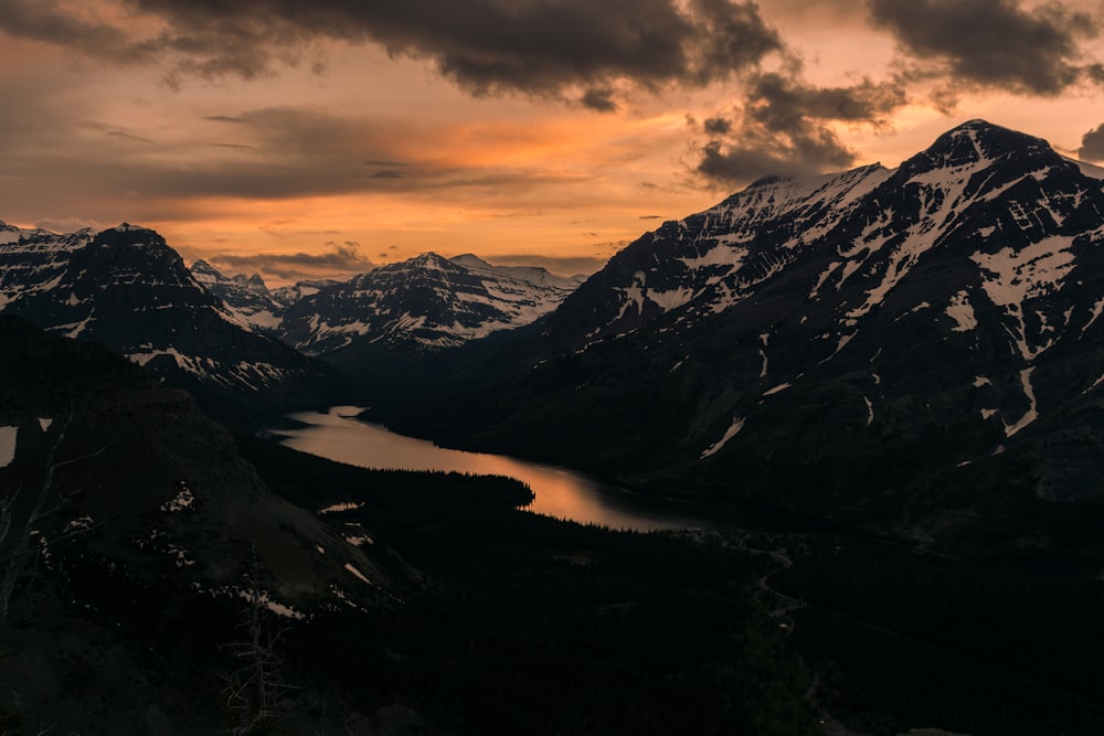 body of water surrounded by black and white mountains under gray sky at golden hour