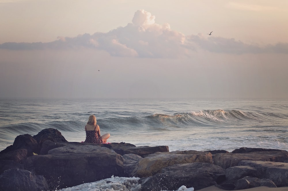 woman sitting on rock near body of water during daytime