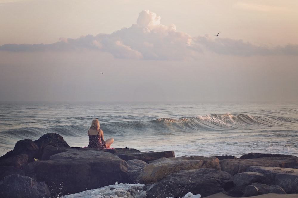 femme assise sur un rocher près d’un plan d’eau pendant la journée