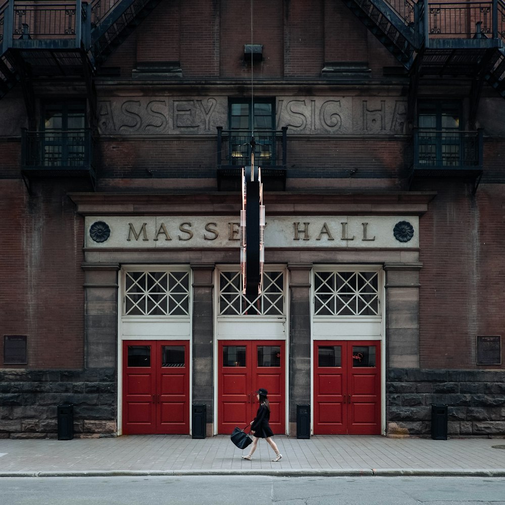 woman walking on street near red Masse Hall during daytime