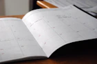 A calendar and tracker sheets laid out on a desk with a pen, ready for planning progress