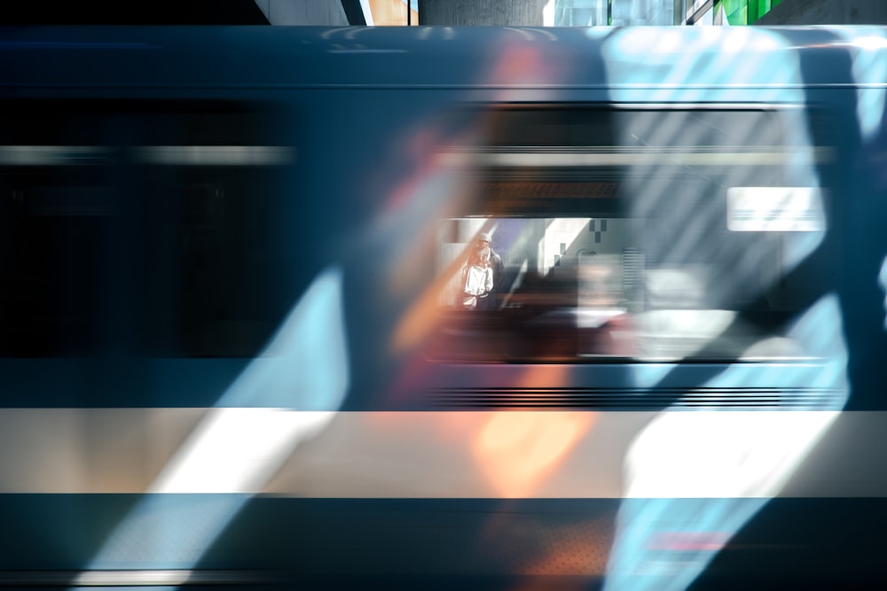 Un wagon de train bleu qui passe brièvement encadrant une personne qui attend