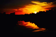 Sunset casting warm hues over the tranquil water hazard reflecting the sky’s colors.