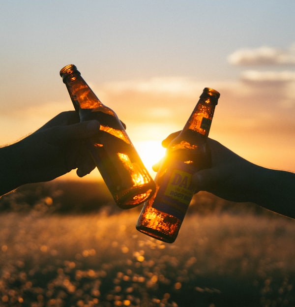 photography of person holding glass bottles during sunset