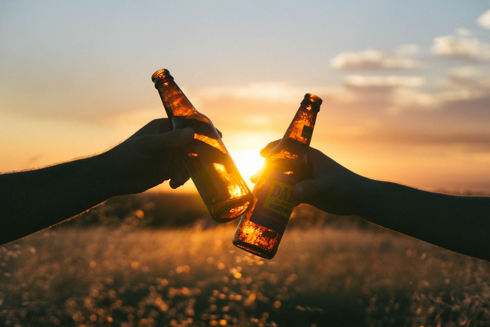 Fotografía de una persona sosteniendo botellas de vidrio durante la puesta del sol