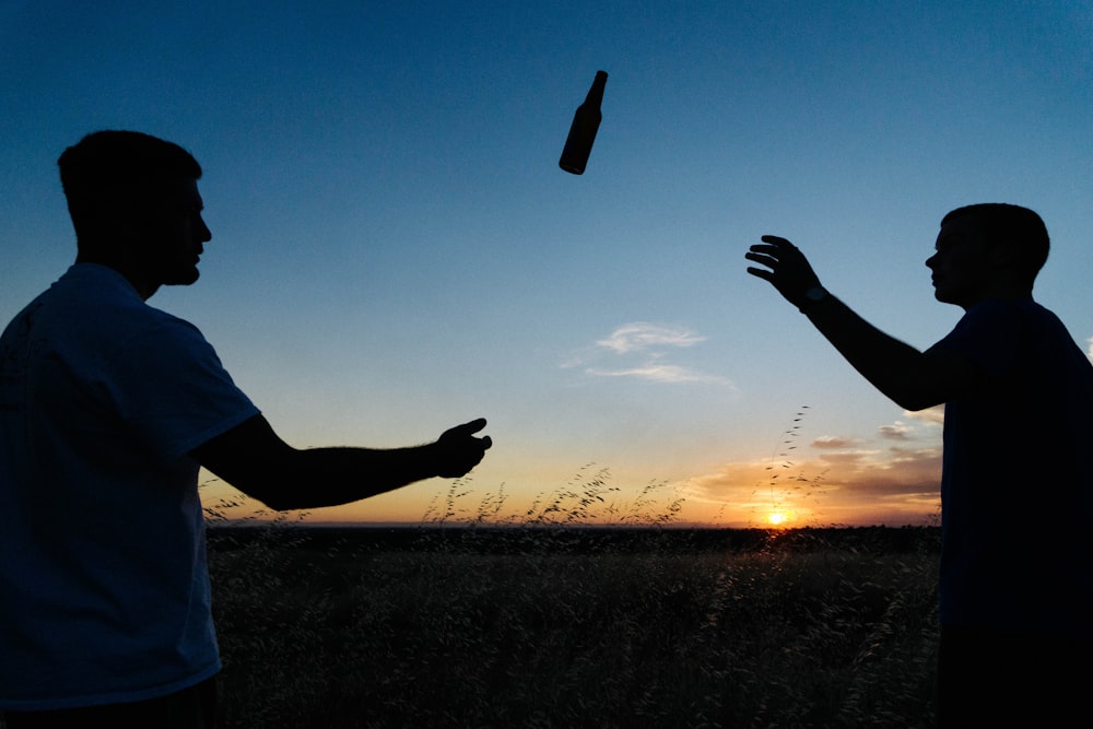 Foto da silhueta de dois homens jogando garrafa durante o dia