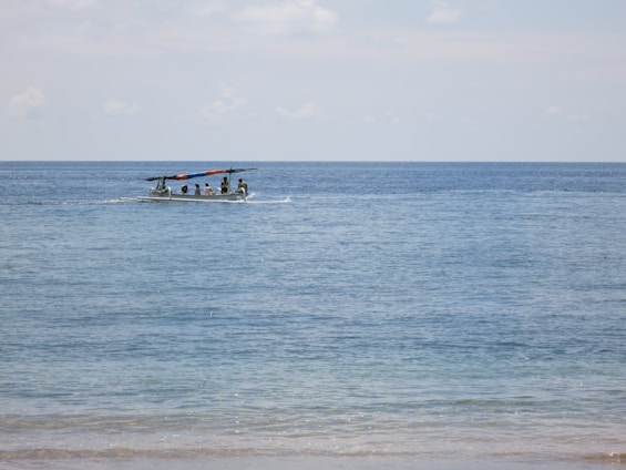 A boat approaching a group of whales in clear ocean waters under a bright sky.