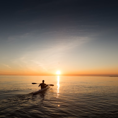 man riding kayak on water taken at sunset