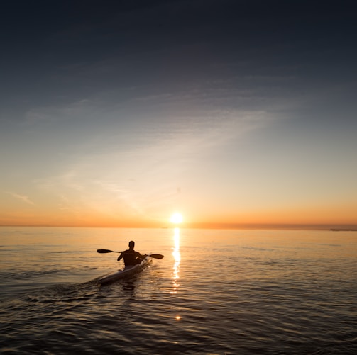 man riding kayak on water taken at sunset