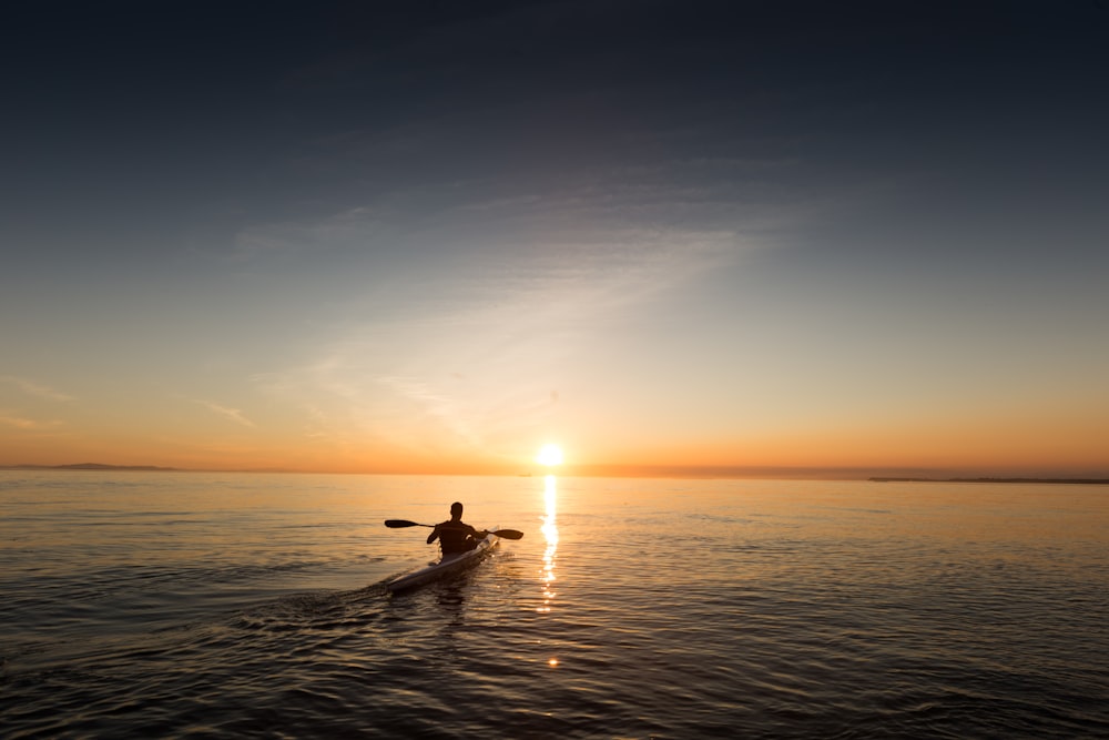 uomo che cavalca il kayak sull'acqua presa al tramonto