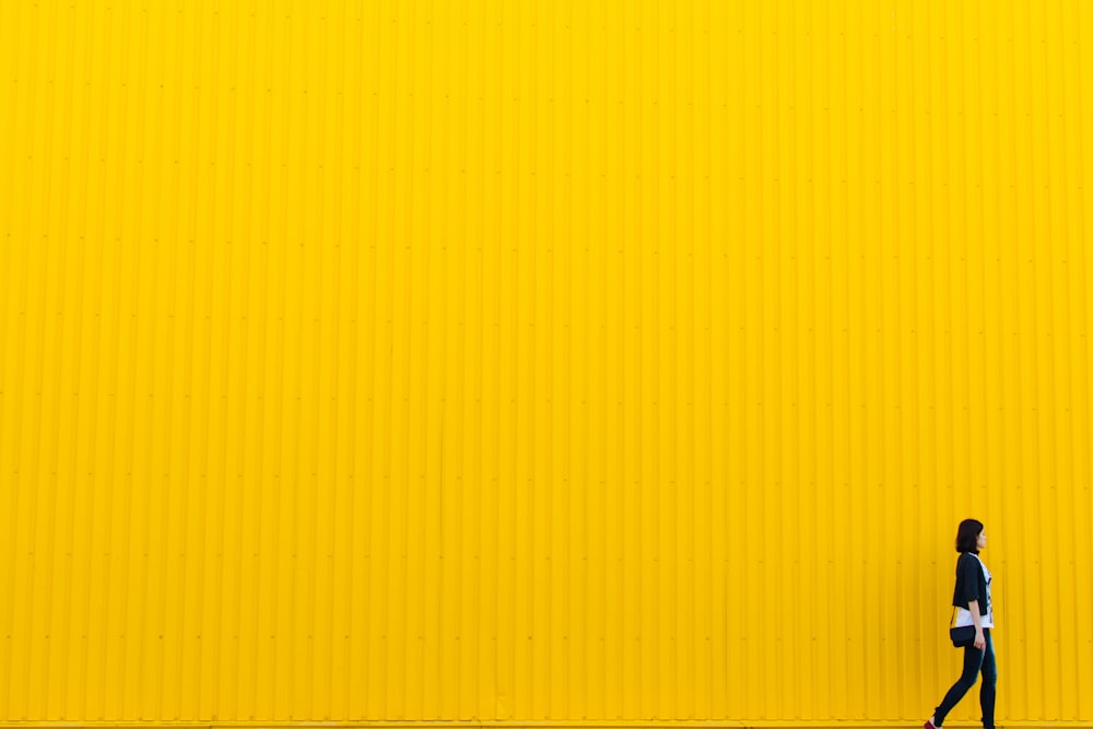 黄色の壁の近くに立っている黒のトップを着ている女性
