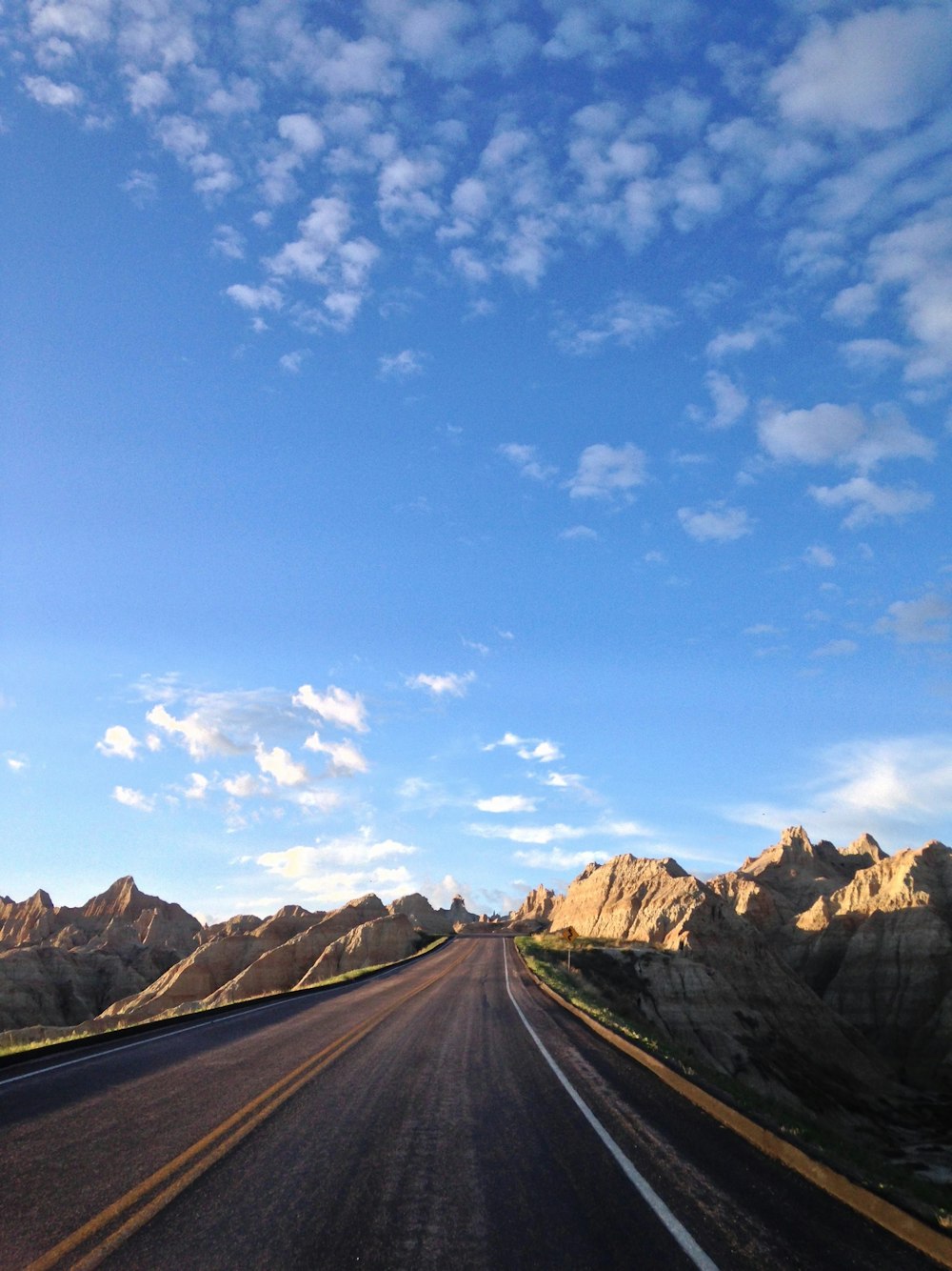 calm concrete road surrounded by rocky mountains during daytime