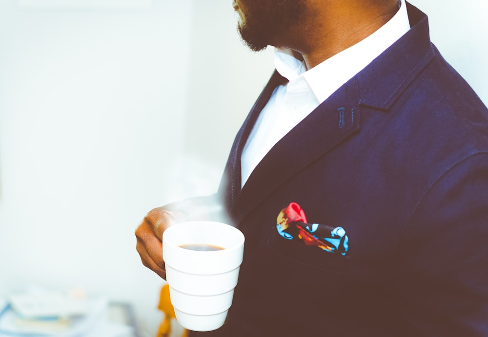 homem segurando caneca de cerâmica branca com café