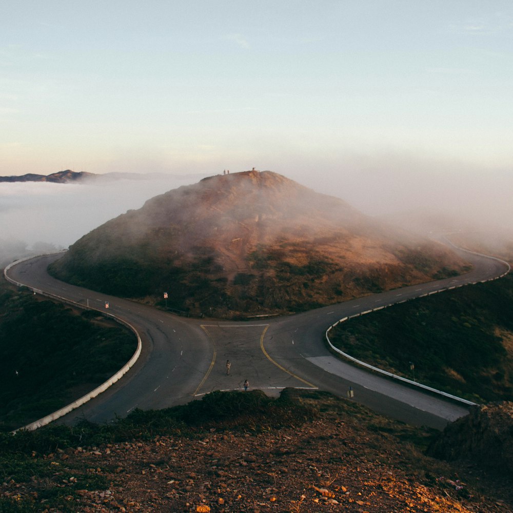 bird's-eye view photo of two people standing on gray concrete road in front of hill