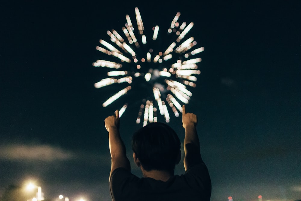 man in black shirt pointing towards brocade fireworks in the skies