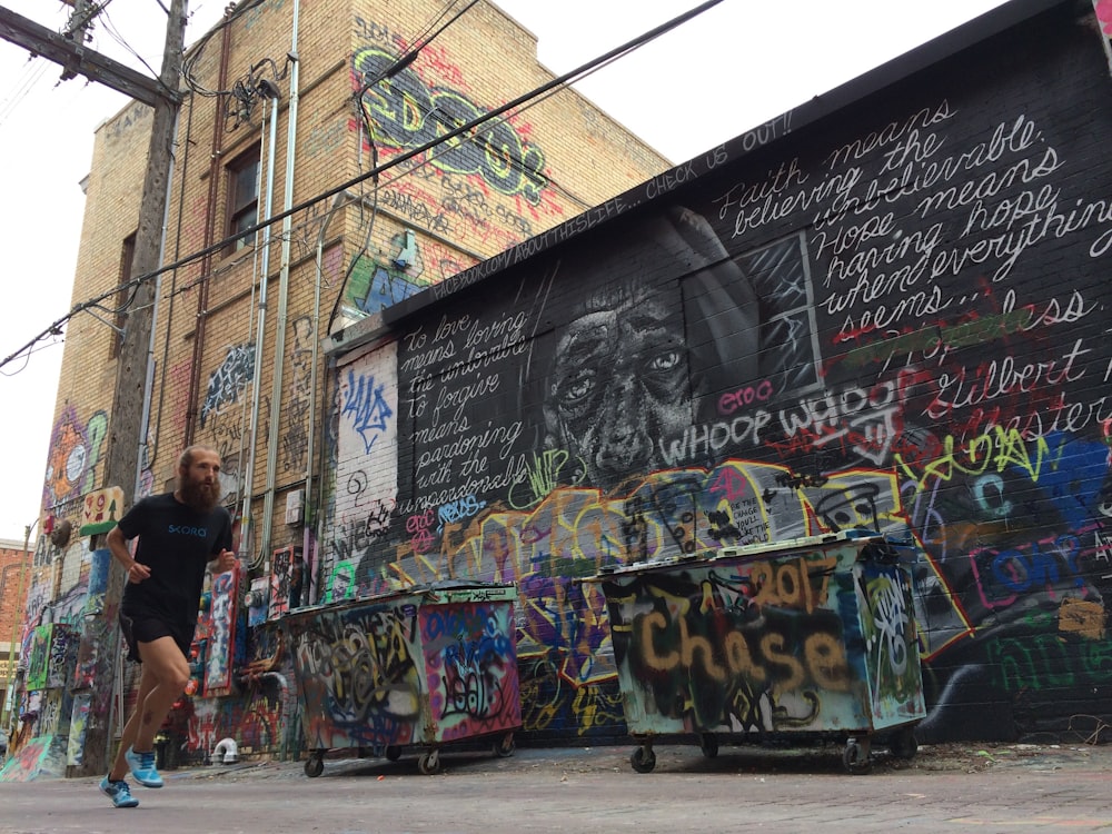 homme en chemise noire courant près du mur avec des graffitis