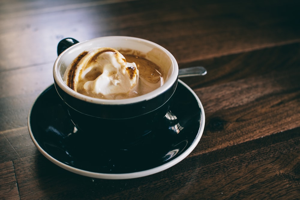 Taza de cerámica blanca y negra llena de café con leche marrón sobre platillo redondo de cerámica negra