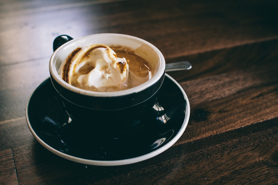 white and black ceramic mug filled with brown latte on round black ceramic saucer, Black coffee cup