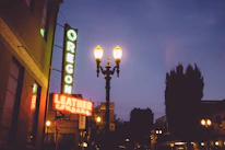 Close-up of colorful neon sign shaped like Oregon glowing pink and black against a dark backdrop.