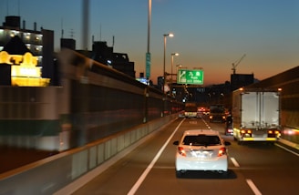 A brightly lit car carrier truck loaded with various vehicles cruising along a highway at dusk.