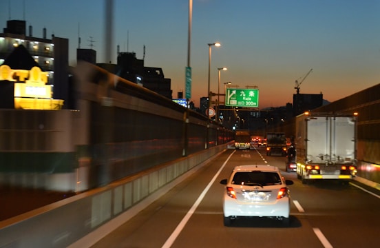A brightly lit car carrier truck loaded with various vehicles cruising along a highway at dusk.