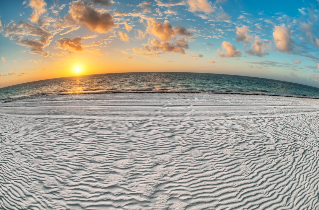 gray sand near body of water under white and blue sky at sunrise