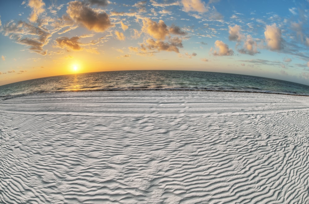 日の出の白と青の空の下の水域近くの灰色の砂浜