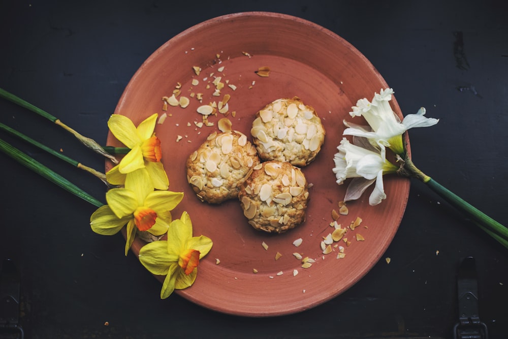 drei runde Kekse auf braunem Teller mit Blütenblättern