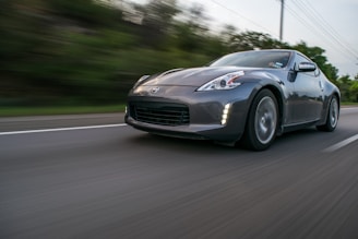 A sleek, dark-colored sports car driving at high speed on a highway with blurred surroundings, emphasizing motion. The car is captured from a low angle enhancing its dynamic and aggressive design.