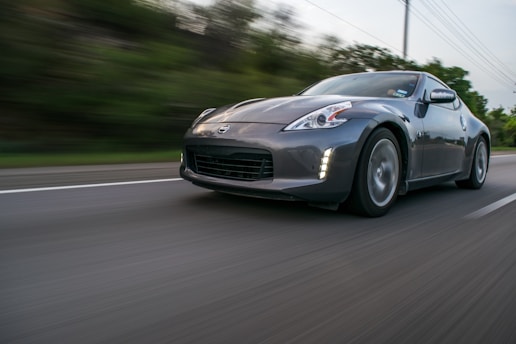 A sleek, dark-colored sports car driving at high speed on a highway with blurred surroundings, emphasizing motion. The car is captured from a low angle enhancing its dynamic and aggressive design.