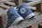 A pair of worn blue Converse All Star sneakers are placed on a wooden pallet. The shoes are tilted sideways showing the iconic logo. The surface appears rustic, adding a vintage feel.