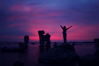 person standing on rock formation with arms in air