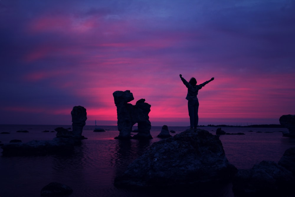 person standing on rock formation with arms in air