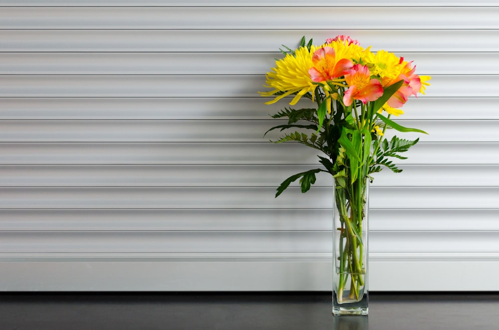 flor de pétalas amarela e vermelha em vaso de vidro transparente