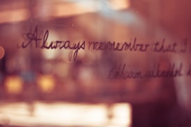 Handwritten text is visible on a reflective glass surface, with a soft focus and warm lighting that creates a cozy and intimate atmosphere. The background appears blurred, with hints of white and orange tones blending smoothly.