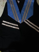 A black graduation gown with a blue stole featuring silver stripes laying on a surface.