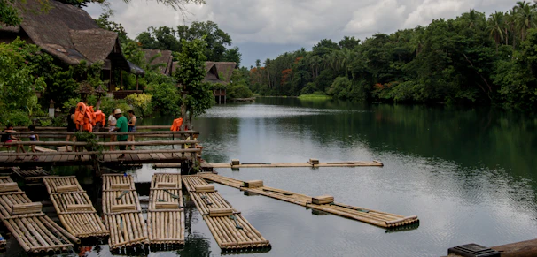 A serene riverside tribal village with artisans weaving colorful textiles under tall trees.