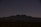 A mountainous silhouette is visible against a dark, starry night sky. The landscape below appears rugged, with sparse vegetation typical of a desert environment.