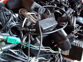 A tangled assortment of various power adapters and electrical cords, including connectors and plugs, all in a chaotic pile.
