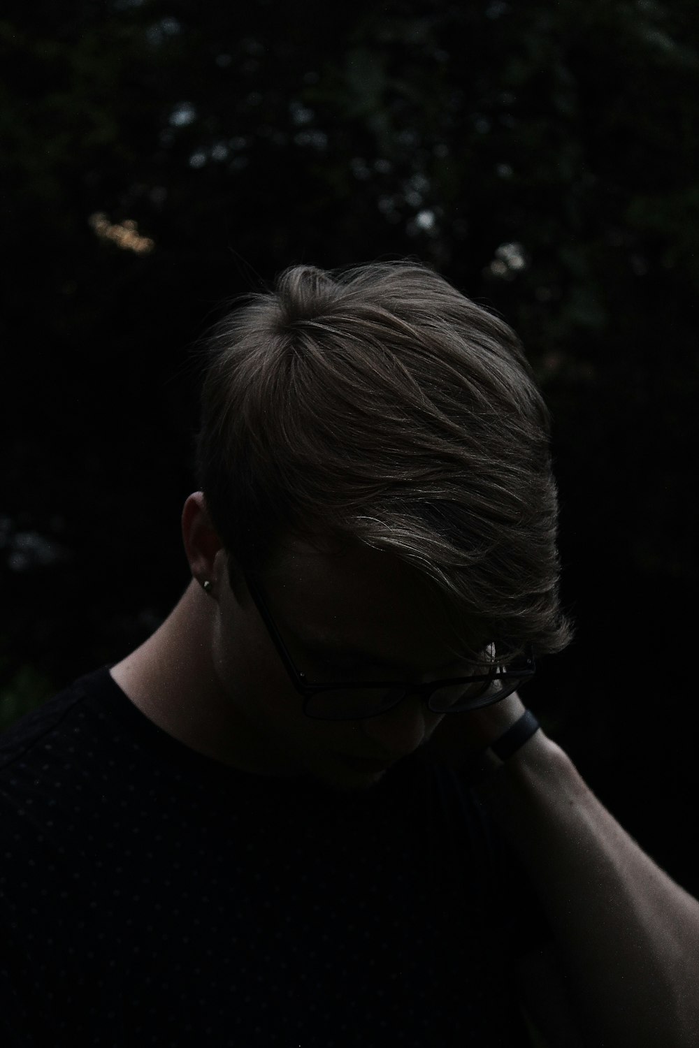 man wearing black shirt and eyeglasses with left hand on neck